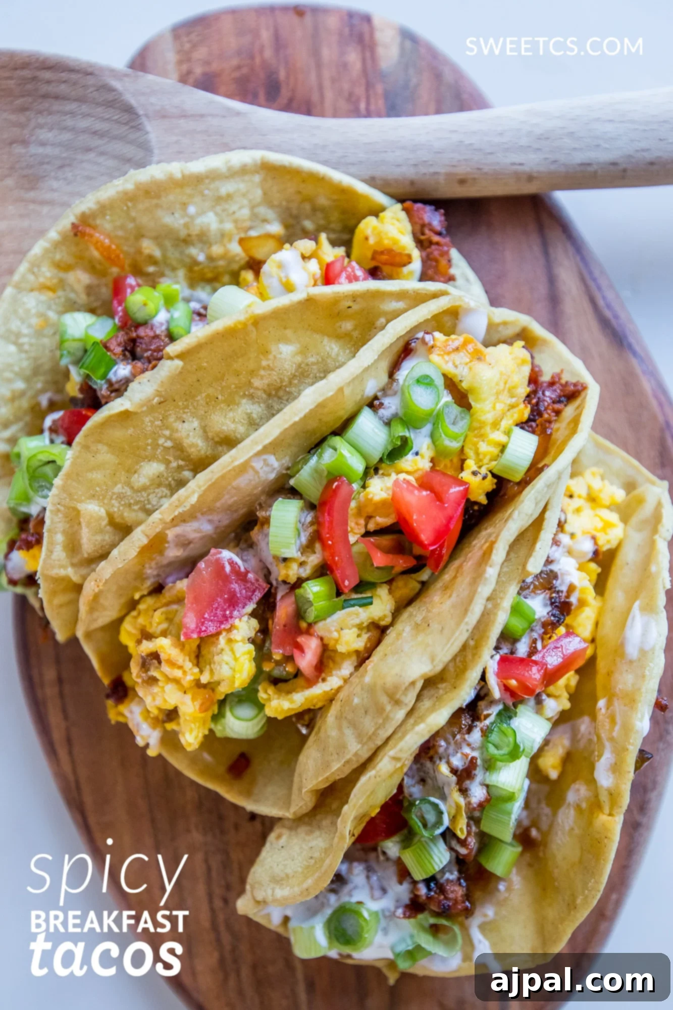 Close-up of a rustic wooden cutting board piled high with spicy breakfast tacos, featuring scrambled eggs, chorizo, and fresh toppings.
