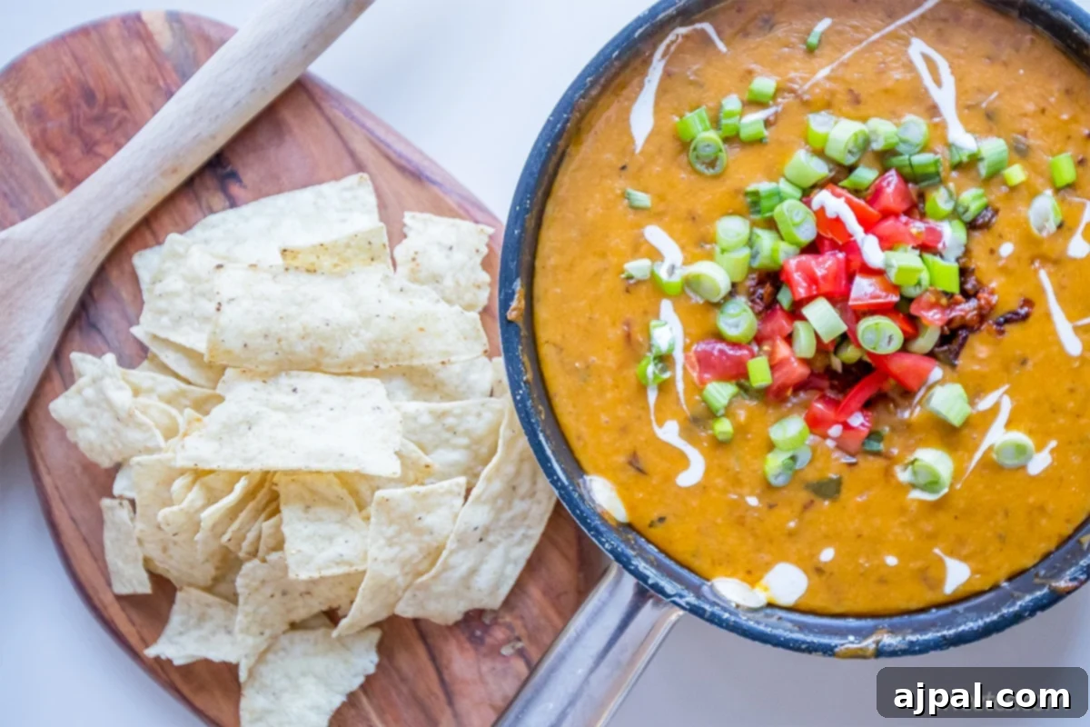 Sizzling Linguica Queso Skillet 2 A vibrant bowl of spicy linguica queso dip, adorned with fresh chiles, bell peppers, green onions, and a dollop of crema. Tortilla chips are arranged on the side, inviting you to dive in.