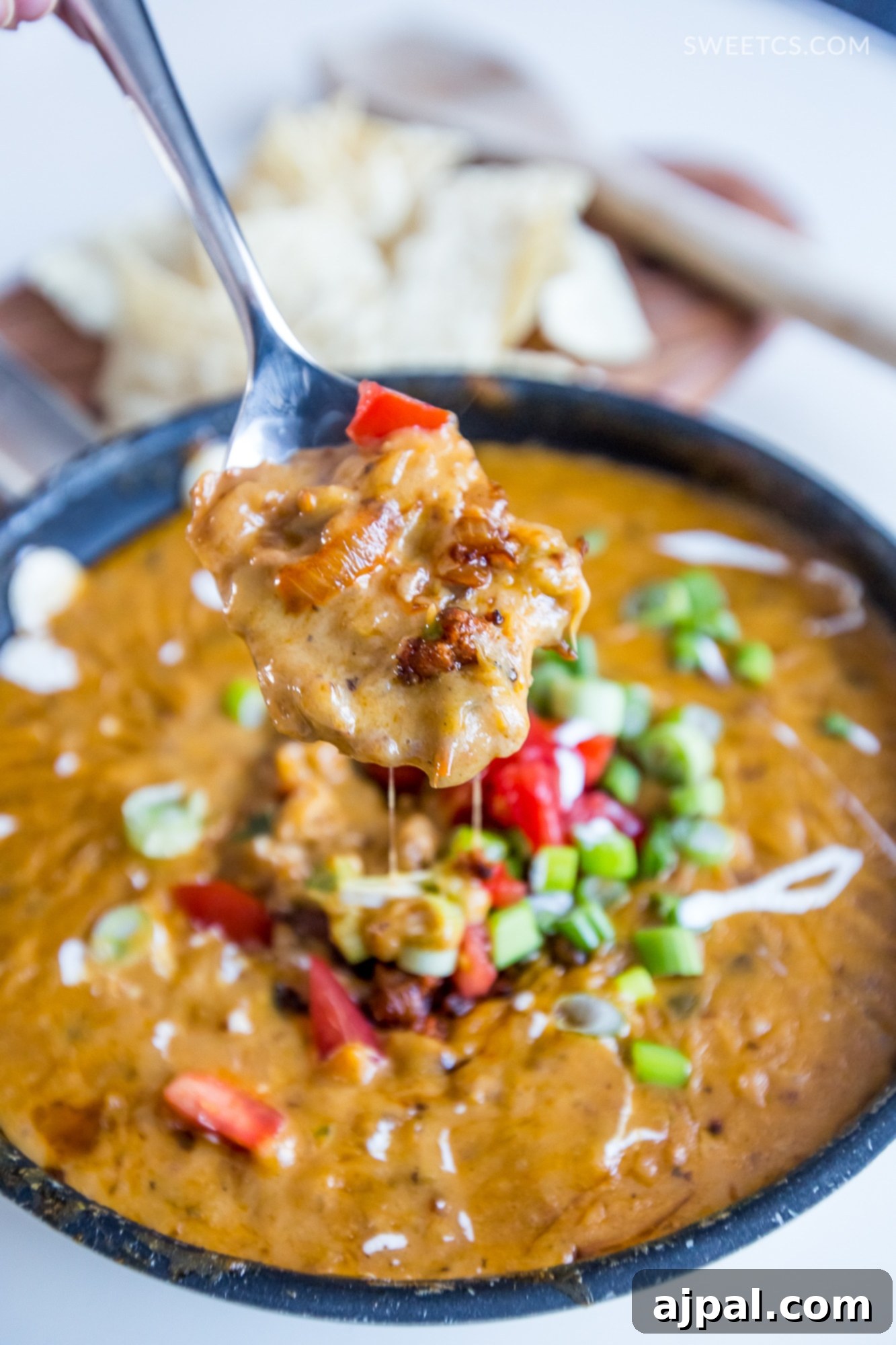 Sizzling Linguica Queso Skillet 5 A person scooping a generous portion of spicy linguica queso dip from a skillet, highlighting its rich and creamy texture, with fresh toppings visible.