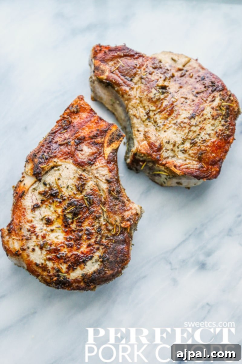 Aromatic Herbs de Provence Pork Chops 2 Perfectly cooked Herbs de Provence Pork Chops garnished with fresh herbs on a marble countertop, ready to serve.