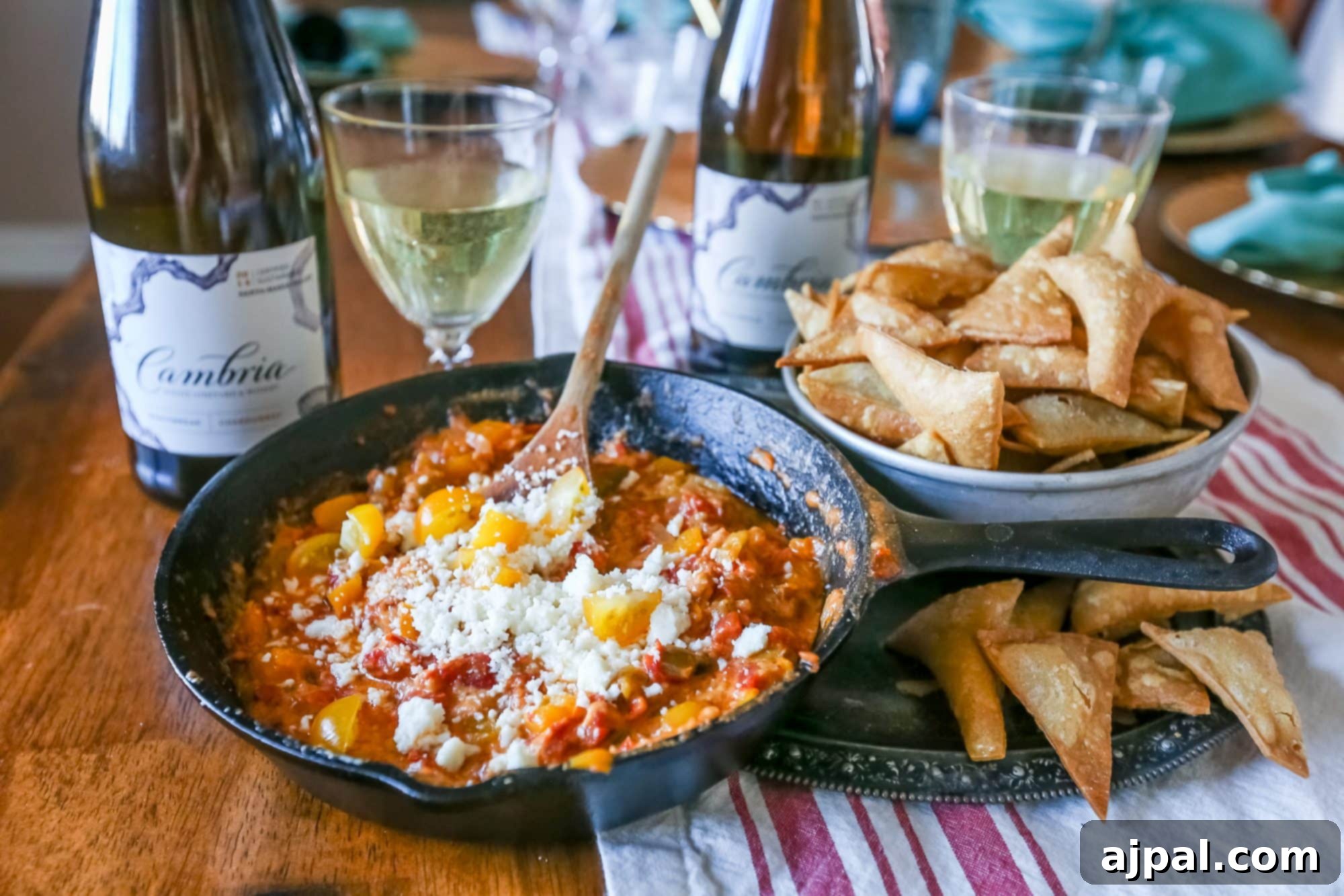 Crispy Homemade Tortilla Chips with Zesty Green Chile Cheese Dip 2 A vibrant skillet of cheesy green chili and bell pepper dip, surrounded by a generous pile of golden homemade tortilla chips and a bottle of Cambria wine, ready for a delicious game day.
