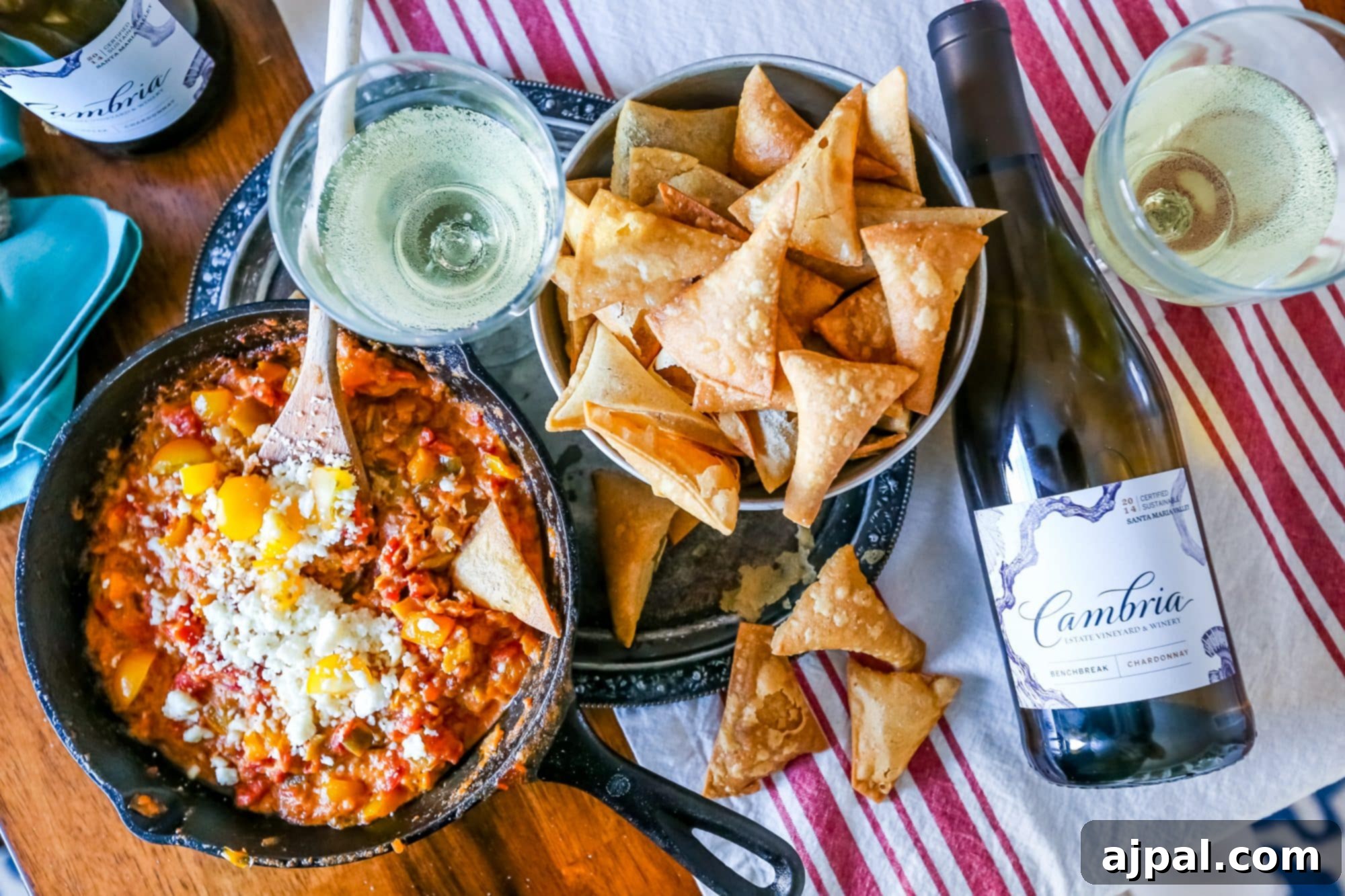 Crispy Homemade Tortilla Chips with Zesty Green Chile Cheese Dip 4 A tantalizing close-up of a bubbling, cheesy green chili and pepper dip in a rustic cast-iron skillet, adorned with fresh cilantro, surrounded by a pile of homemade tortilla chips and a bottle of Cambria wine.