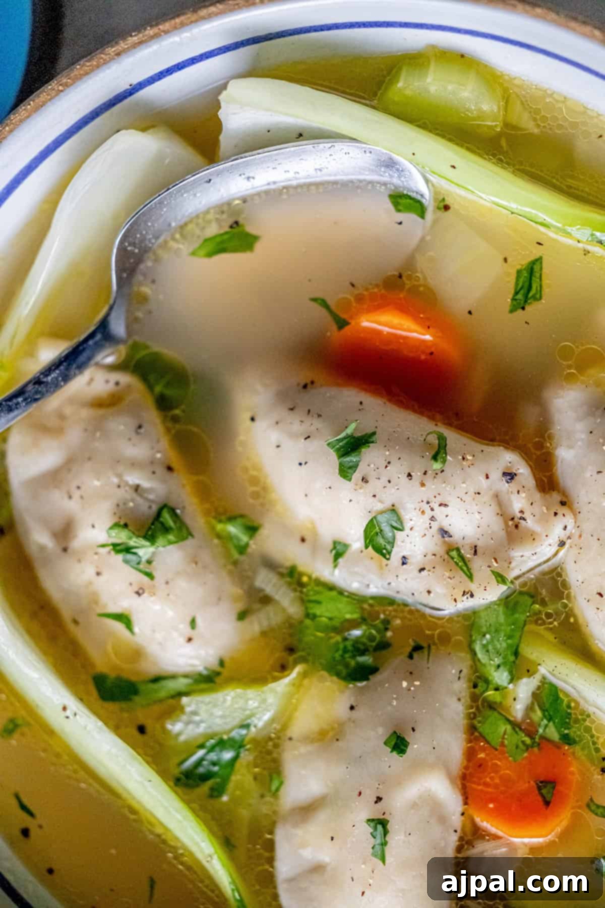 Easy 15-Minute One-Pot Potsticker Soup 13 A bowl of 15-minute potsticker soup brimming with chicken dumplings, carrots, and greens. A spoon rests in the comforting broth where the surface is dotted with herbs and pepper.