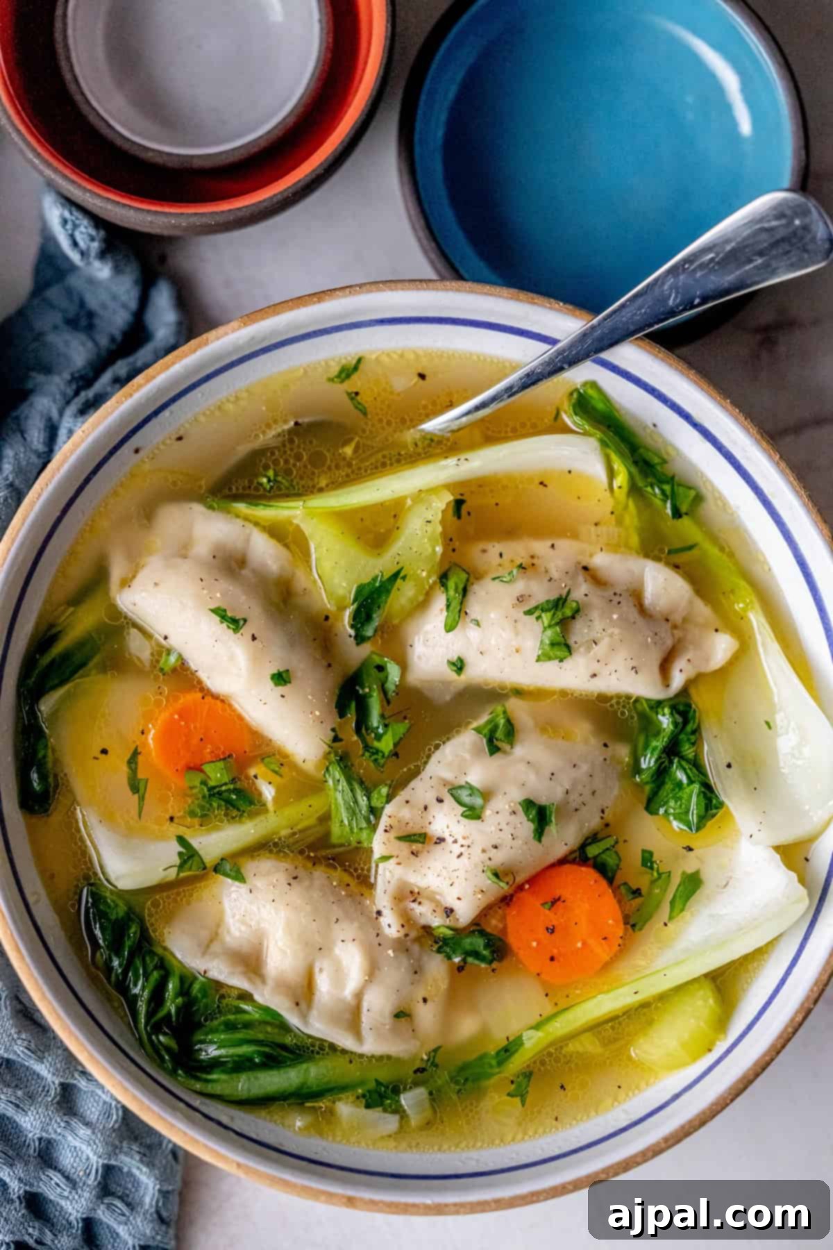 Easy 15-Minute One-Pot Potsticker Soup 4 A bowl of 15-minute potsticker soup brimming with dumplings, bok choy, sliced carrots, and herbs. A spoon rests on the bowl's edge while two empty bowls await in the background.