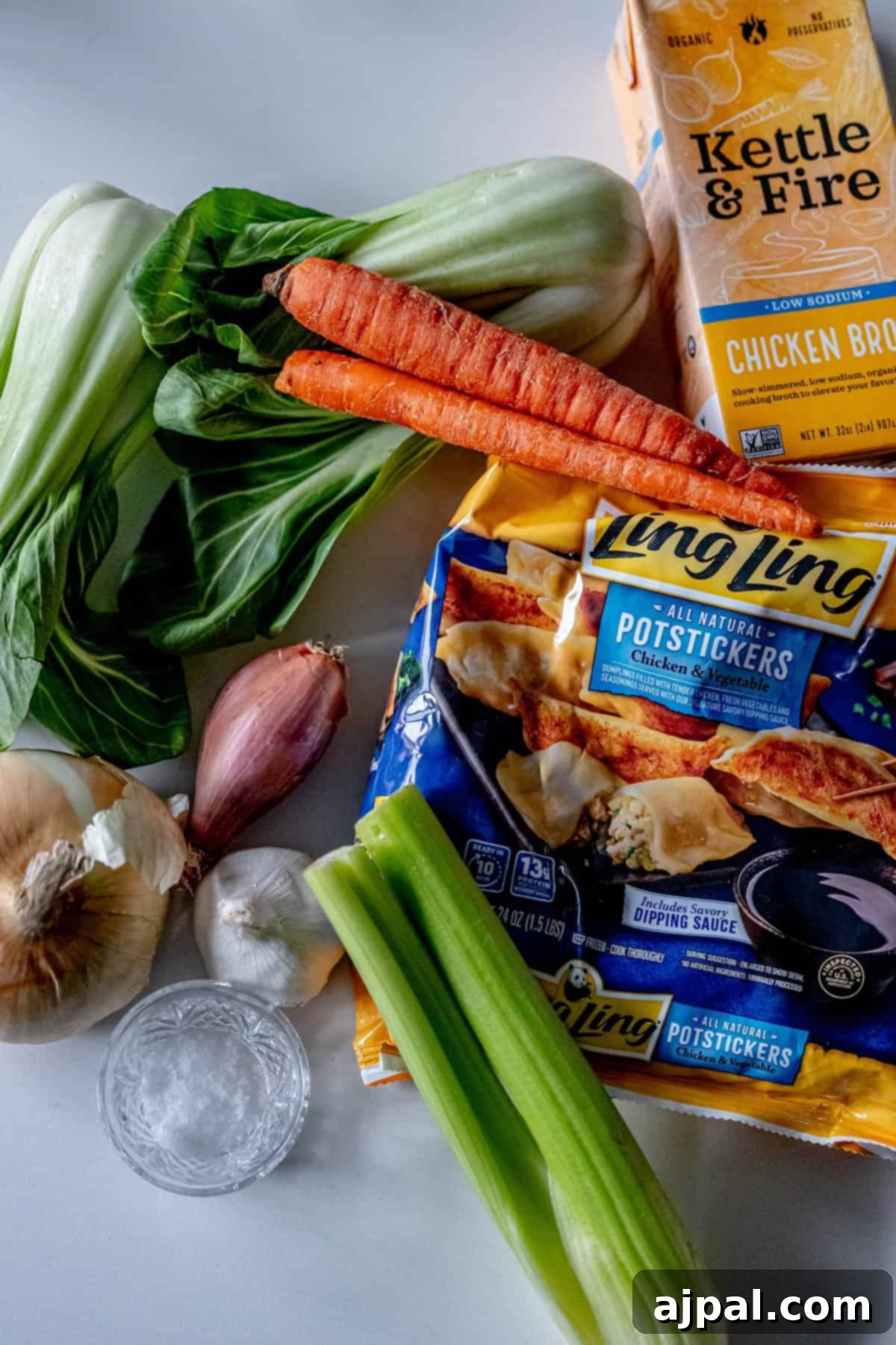 Easy 15-Minute One-Pot Potsticker Soup 5 Ingredients on a counter: bok choy, carrots, onion, shallot, garlic, celery, salt, chicken broth, and packages of chicken and vegetable potstickers. Transform these into a delightful 15-minute potsticker soup that brings warmth and flavor to your table in no time.