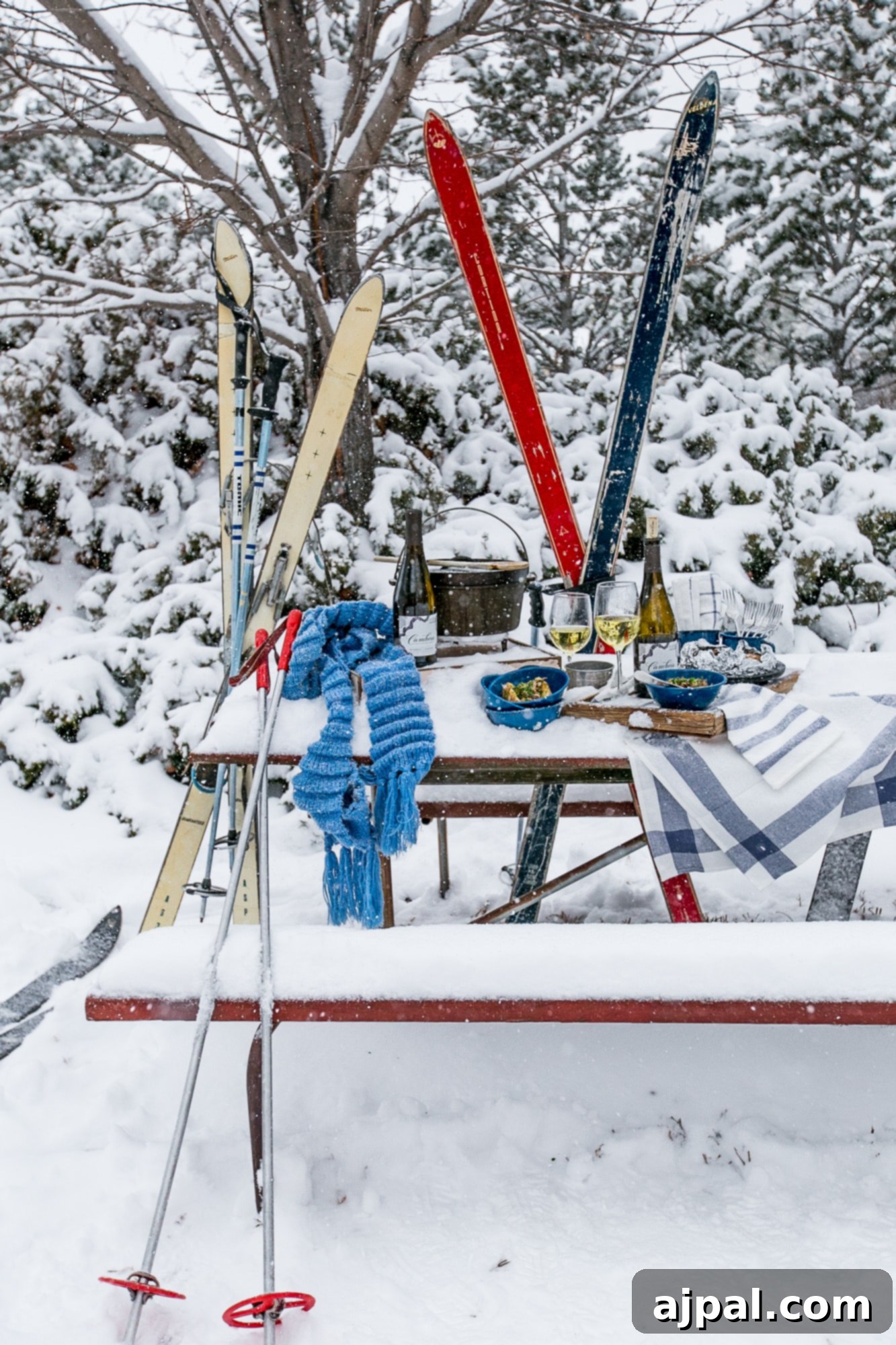 A charming picnic table covered in snow, featuring skis and bowls of country rib stuffed potatoes in a picturesque winter country setting.