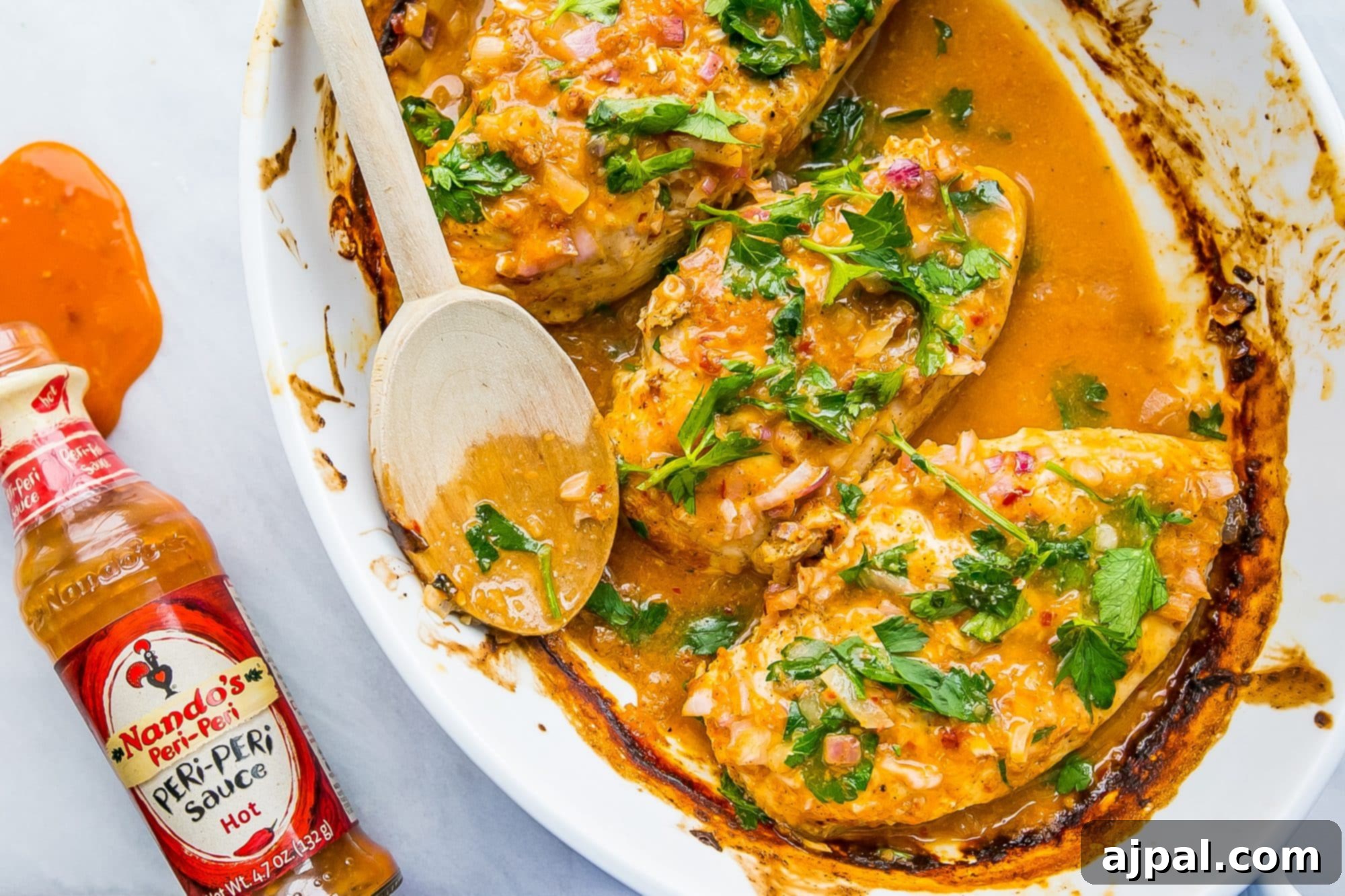 Easy 3 Ingredient Nandos Peri Peri Chicken 4 chicken in a pot with red sauce and fresh parsley on it, peri peri sauce hot on the side