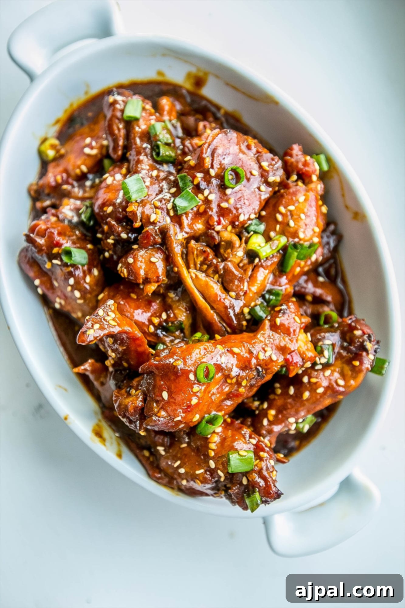 Sticky Honey Soy Slow Cooker Chicken Wings 3 A close-up of honey soy wings served in a white bowl, garnished with green onions and sesame seeds.