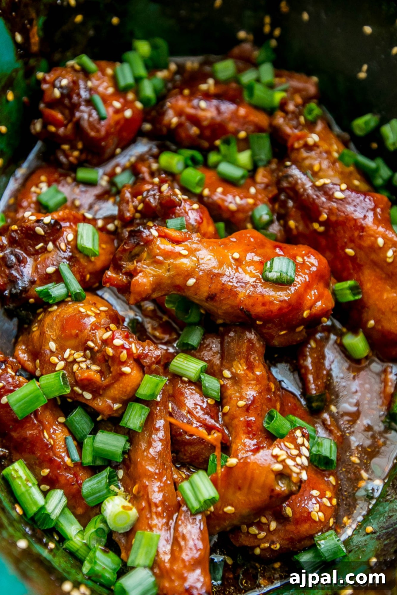 Sticky Honey Soy Slow Cooker Chicken Wings 5 A serving of sticky Asian chicken wings, garnished with sesame seeds and fresh green onions in a bowl.