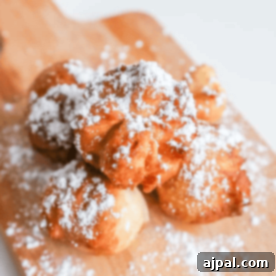 Golden Peanut Butter Jelly Poppers 7 Powdered doughnuts on a wooden cutting board next to 3 Ingredient Fried Peanut Butter Jelly Bombs.