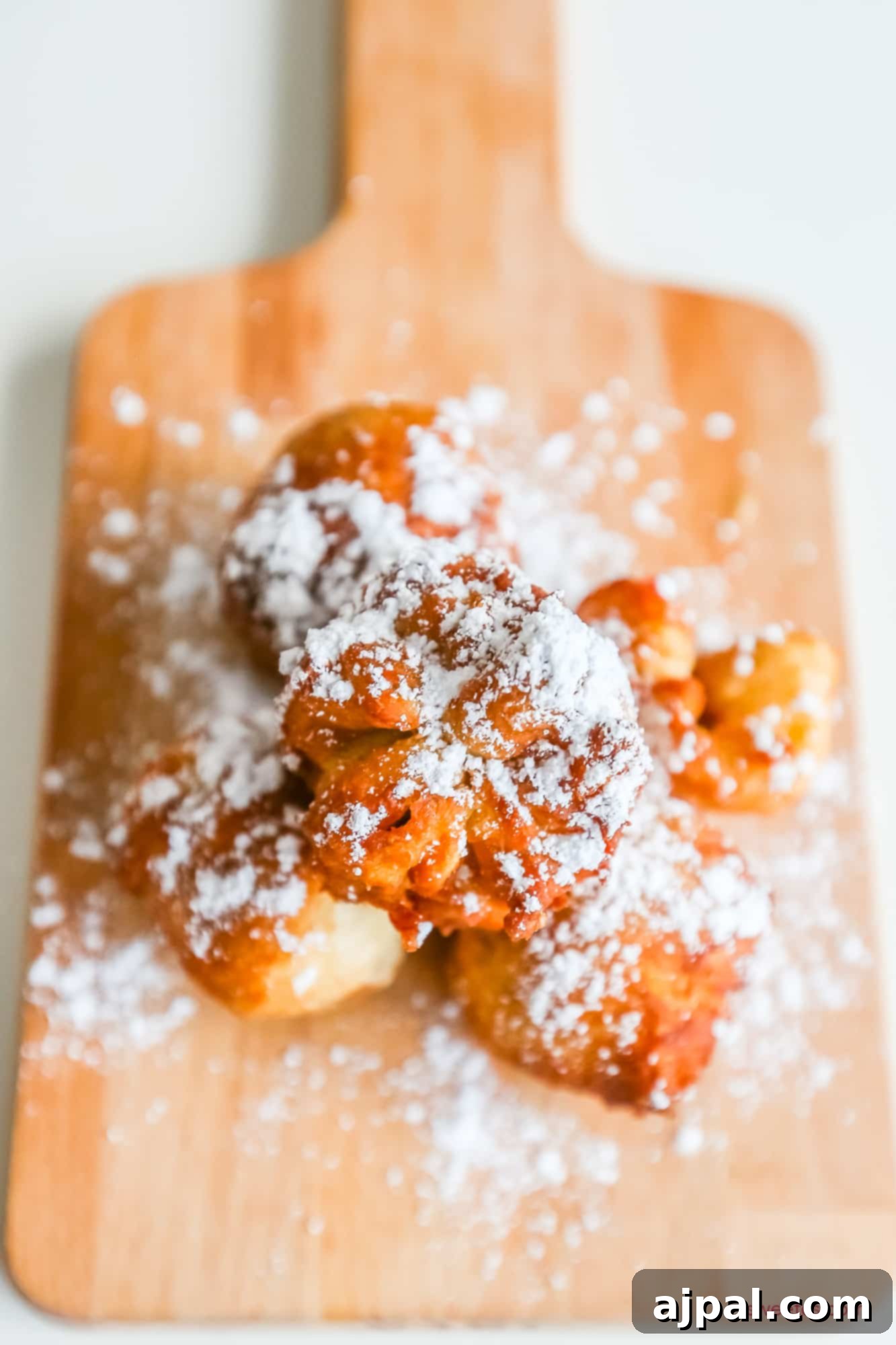 Golden Peanut Butter Jelly Poppers 4 A wooden cutting board laden with powdered donuts, enticingly fried peanut butter and jelly bombs.