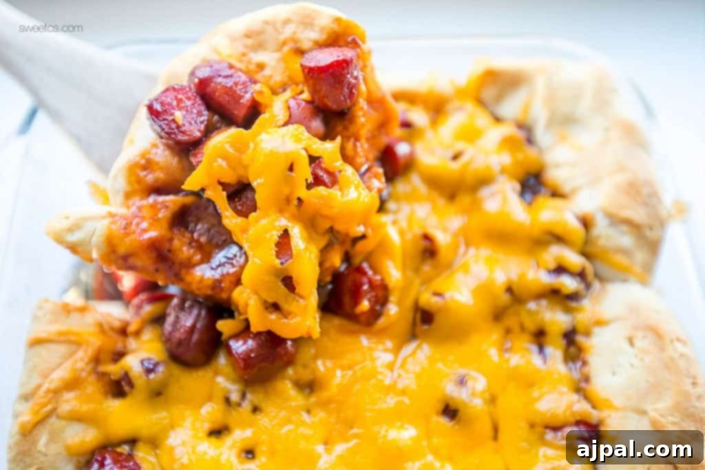 Hearty Cheesy BBQ Smokie Bake 2 wooden spoon lifting biscuits with little smokies sausages and cheese on them