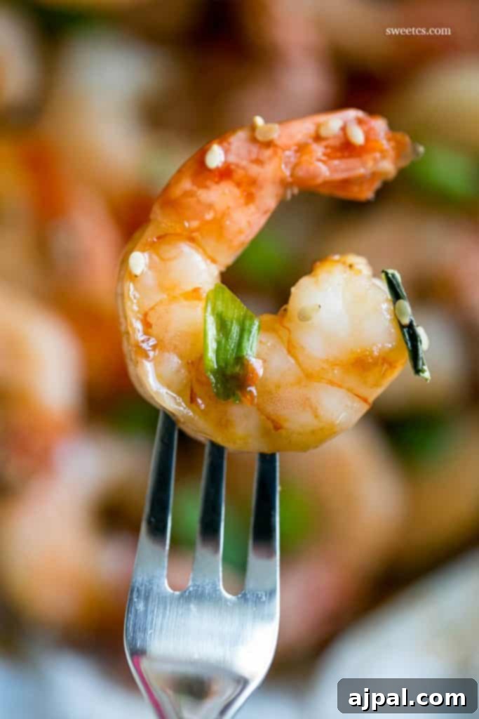 A single honey ginger baked shrimp perfectly placed on a fork, garnished with vibrant green onions, emphasizing its quick, delicious, and gourmet appetizer appeal.