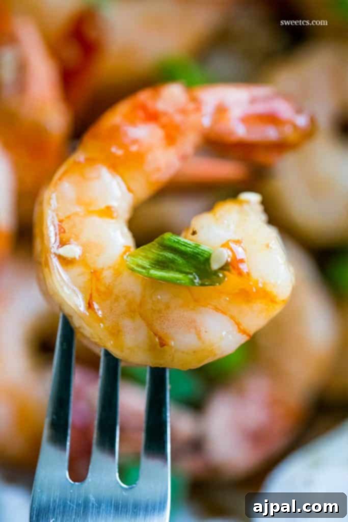 A perfectly cooked honey ginger baked shrimp on a fork, garnished with fresh green onions and sesame seeds, capturing the deliciousness of this easy Asian-inspired recipe.