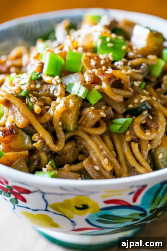 Velvety Tahini Noodles 7 A close-up of creamy vegan tahini noodles topped with sesame seeds, mushrooms, and green onions in a decorative floral bowl.