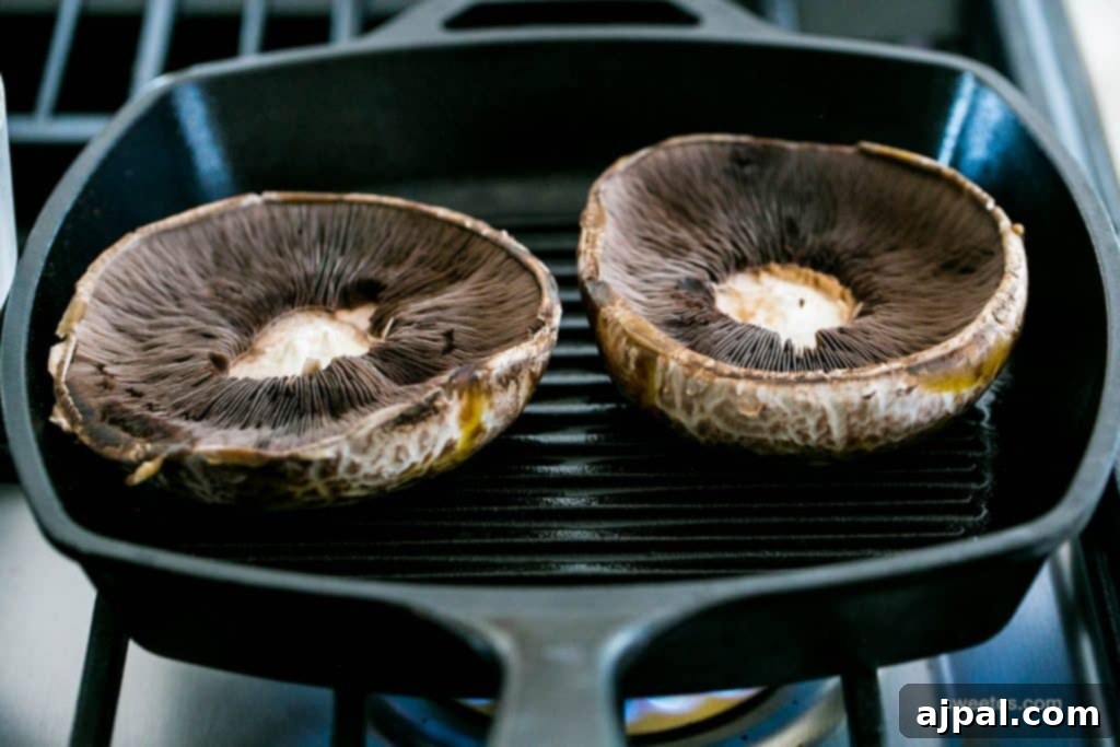 Two large portobello mushrooms sizzling in a cast iron skillet, being cooked to perfection as delicious burger substitutes.