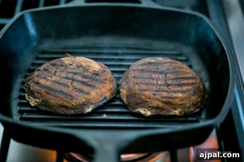 Close-up of two perfectly seared portobello mushrooms, cooked in a cast iron skillet, transforming into delicious, meaty vegan burgers.