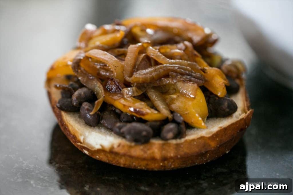 The bottom bun of a spicy Mexican vegan burger, generously topped with a savory mixture of black beans, grilled bell peppers, and caramelized onions.