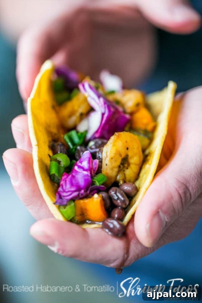 Hand holding a perfectly crafted Habanero Tomatillo Shrimp Taco, bursting with fresh ingredients.