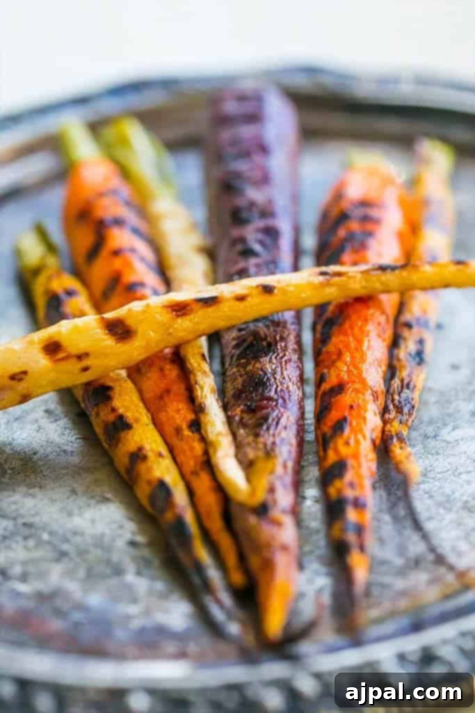 Vibrant, multicolored pan-roasted butter carrots are elegantly arranged on a round metal plate, showcasing their perfect char and appetizing glisten.