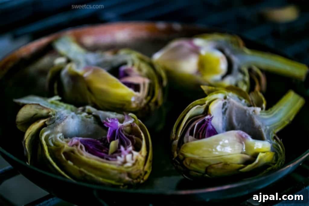 Charred artichokes cooking in a hot pan on the stove, absorbing the rich garlic butter for deep, caramelized flavor.