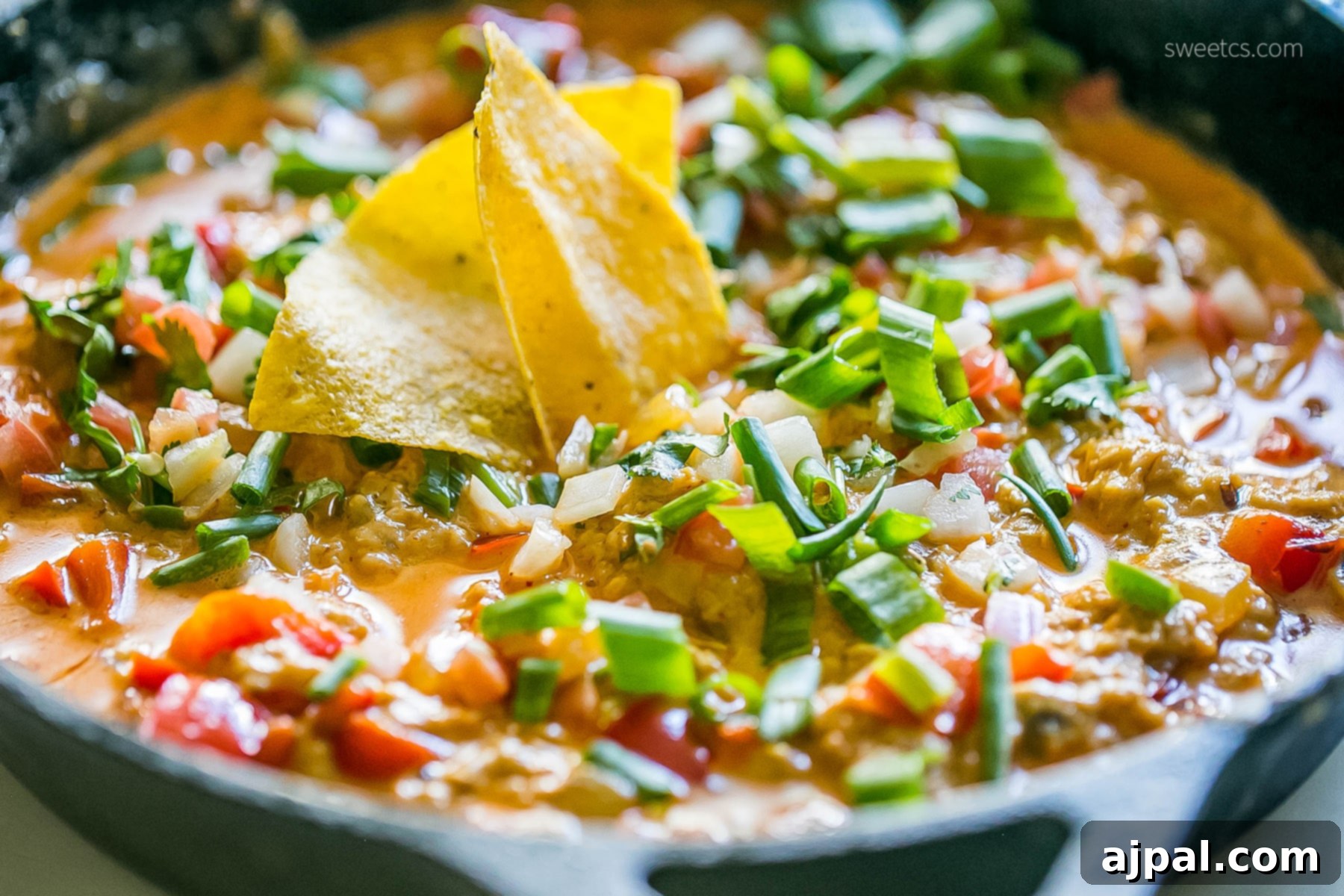 A large skillet filled with cheesy chicken enchilada dip, generously topped with fresh cilantro, diced red onions, and crema, ready to be devoured with tortilla chips.