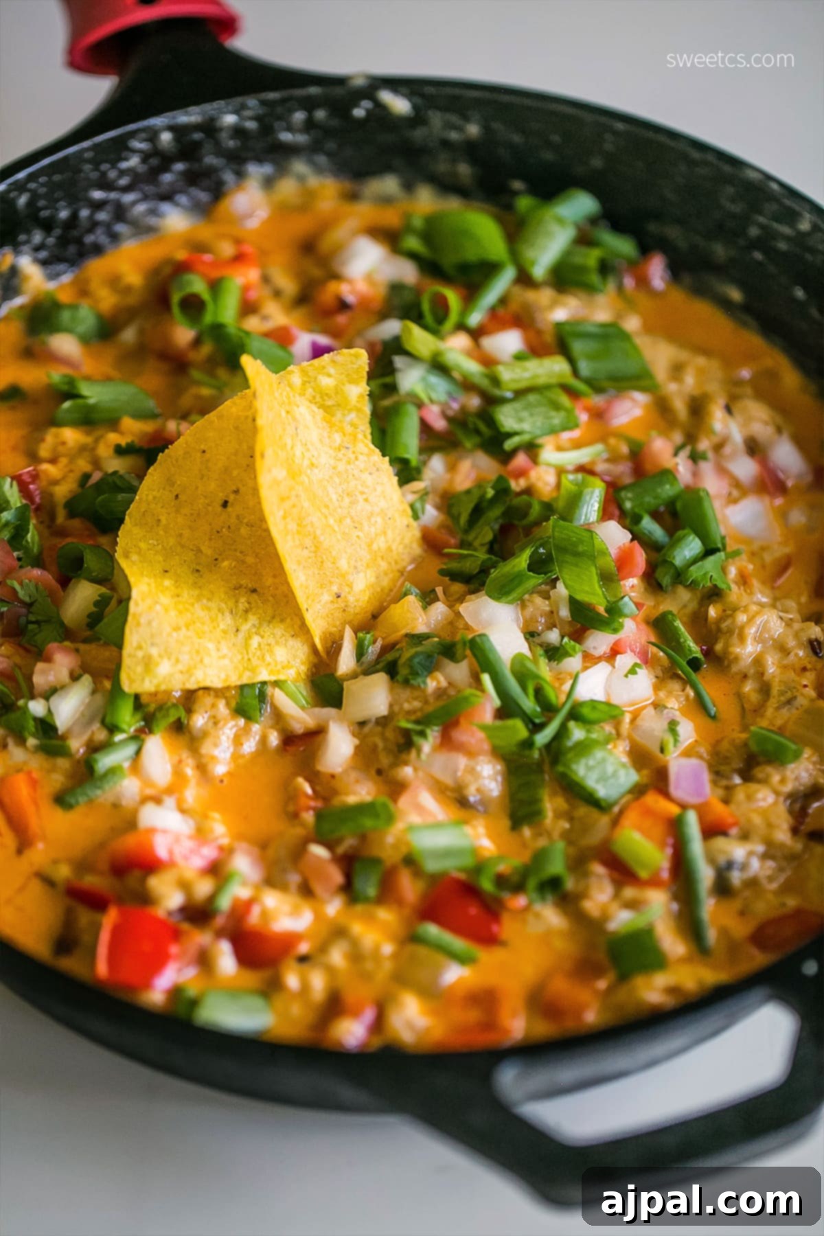 A close-up of cheesy Mexican chili dip, overflowing with ingredients, ready to be enjoyed with a pile of golden tortilla chips.