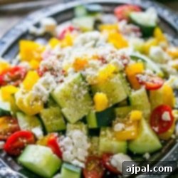 A vibrant close-up of a fresh Garden Vegetable Greek Salad, featuring crisp cucumbers, juicy red tomatoes, bright bell peppers, and crumbled feta cheese, all lightly dressed.