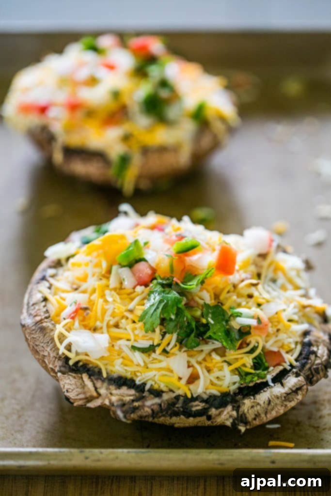 Fiesta Stuffed Mushrooms 3 Unbaked portobello mushroom caps filled with seasoned taco meat, shredded cheese, and vibrant pico de gallo, arranged on a baking sheet.