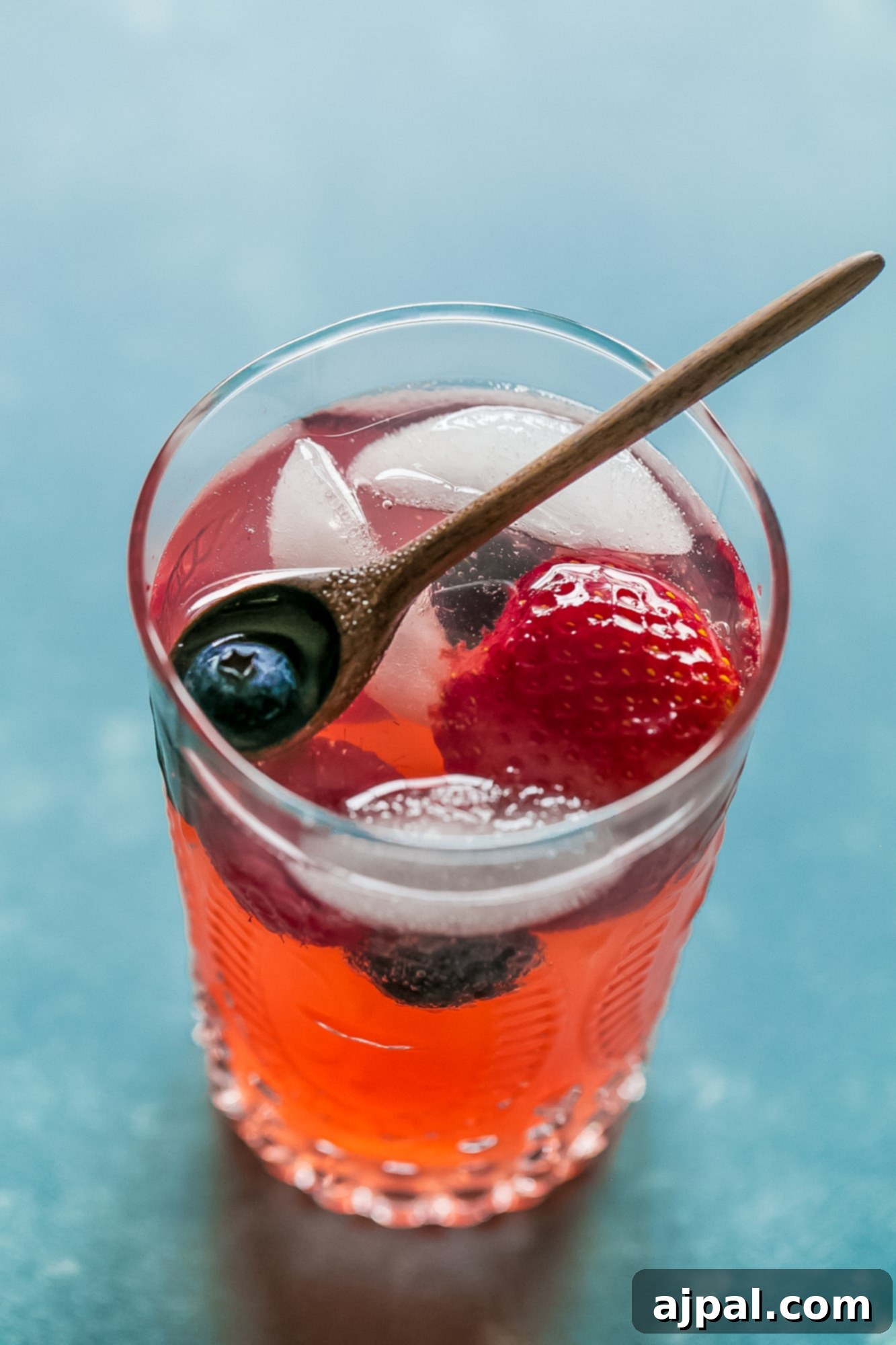 Berry Basil Garden Sparkler 8 A close-up of a wooden spoon holding fresh raspberries and blueberries, ready to be added to a drink or dish.