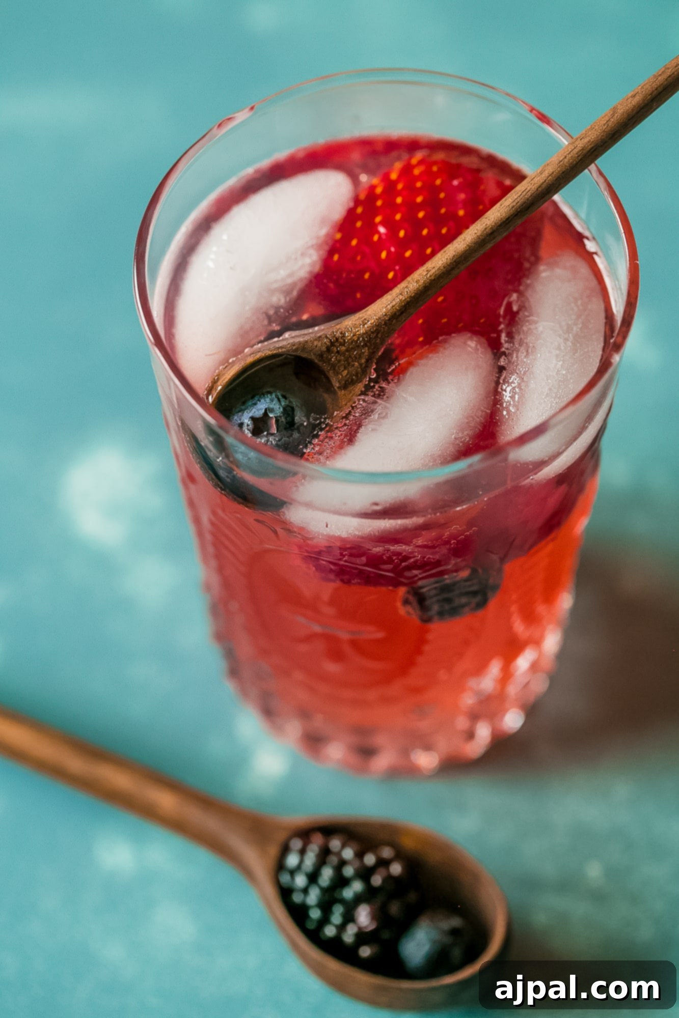 Berry Basil Garden Sparkler 6 A close-up of a glass of sparkling berry basil lemonade with a spoon, highlighting the rich red color and floating fresh berries.