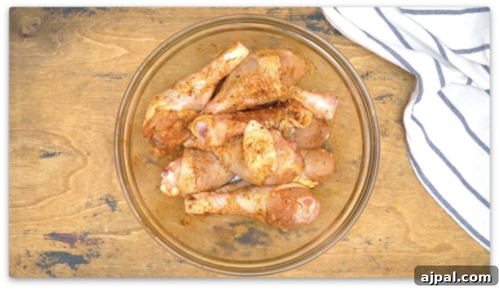 Chicken thighs in a glass bowl on a wooden table, prepared as easy air fried drumsticks using an air fryer.