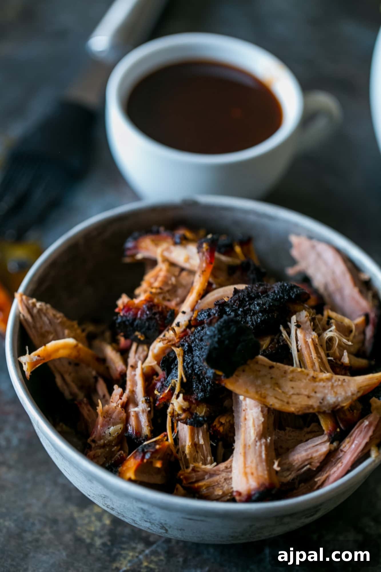 A large bowl filled with perfectly smoked, shredded pulled pork, garnished with fresh herbs, ready to be served.