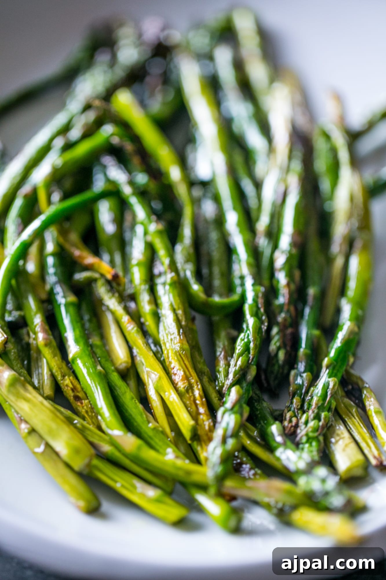Perfectly cooked asparagus spears piled on a white plate, ready to be served as a delicious side dish.
