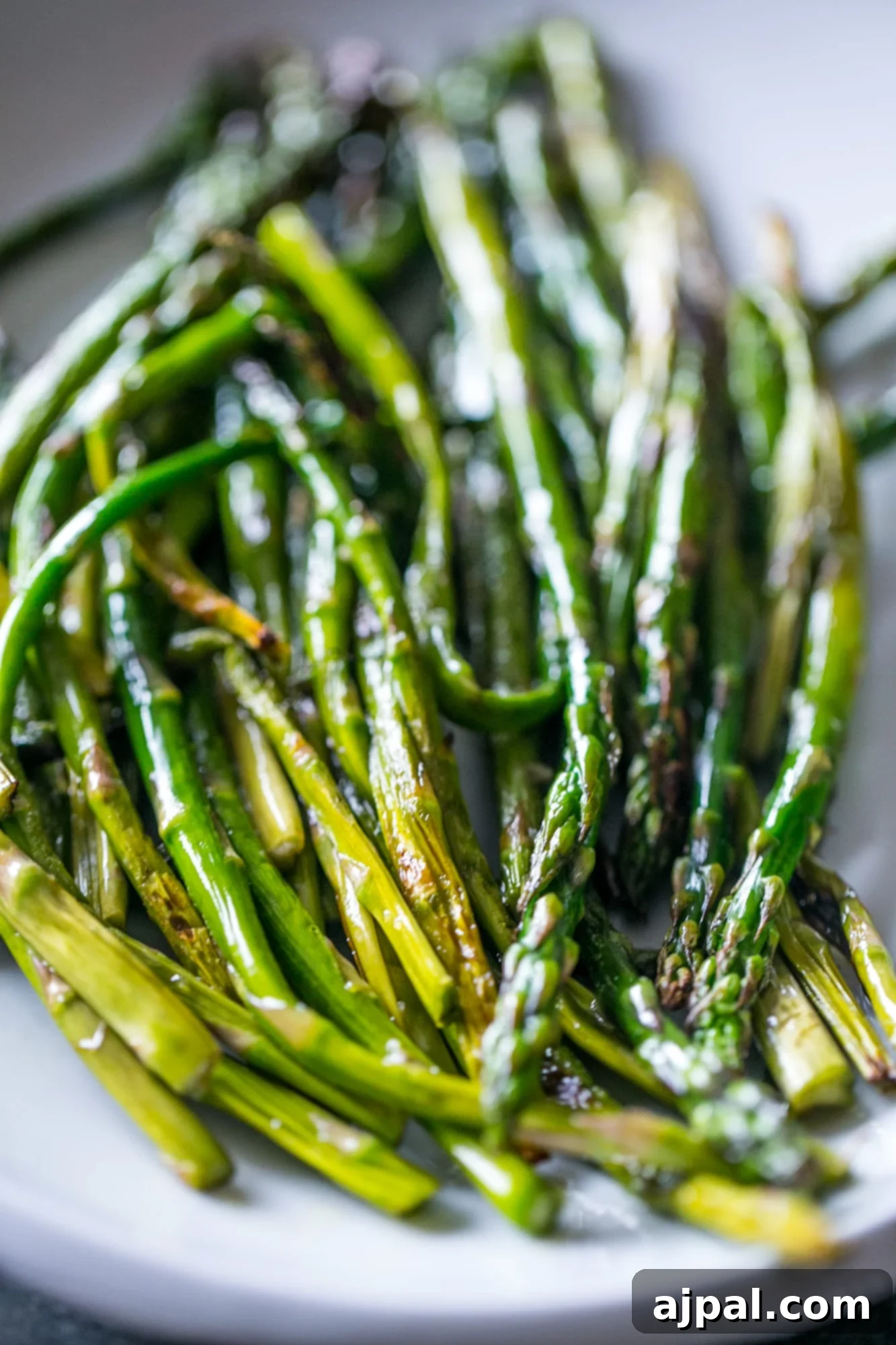 Perfectly Pan-Fried Asparagus 2 Deliciously cooked pan-fried asparagus spears piled on a plate, garnished lightly.