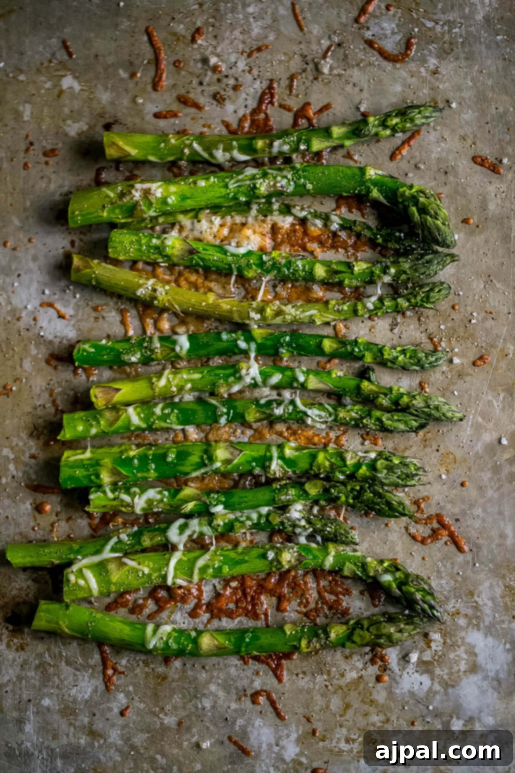 Roasted asparagus on a baking sheet with melted parmesan and garlic