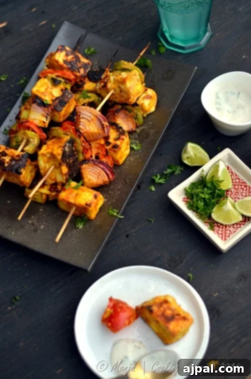 Grilled Tikka Paneer and Vegetable Kebabs 3 paneer and vegetable skewers on a platter with limes and cilantro around it