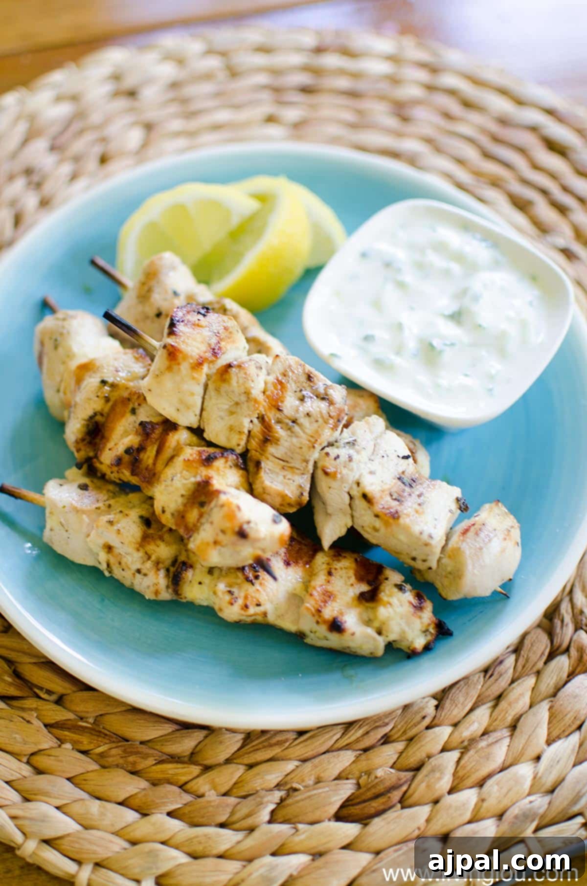 Greek Lemon Herb Chicken Skewers 4 A close-up of authentic grilled Greek chicken souvlaki on a plate, served with lemon wedges and a generous dollop of tzatziki sauce.