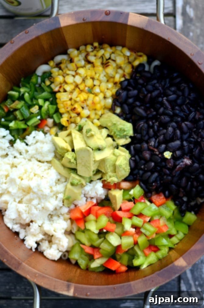 Black Bean & Pasta Salad with Cilantro-Lime Vinaigrette 4 A close-up shot of a large mixing bowl filled with the ingredients for Cilantro Lime Black Bean Pasta Salad, showcasing tender noodles, colorful bell peppers, sweet corn, hearty black beans, creamy avocado, and crumbled cotija cheese, all waiting to be tossed with dressing.