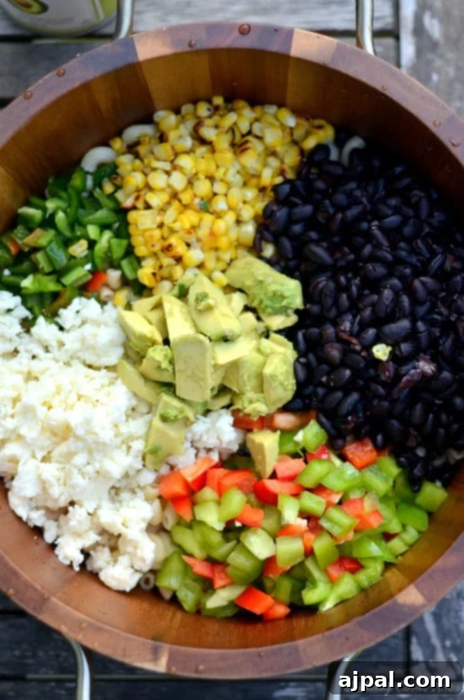 Zesty Cilantro Lime Black Bean Pasta Salad 4 Close-up of a large bowl filled with vibrant corn and black bean pasta salad, showing macaroni, bell peppers, corn, black beans, avocado slices, and crumbled Cotija cheese, all dressed in a creamy cilantro-lime sauce.