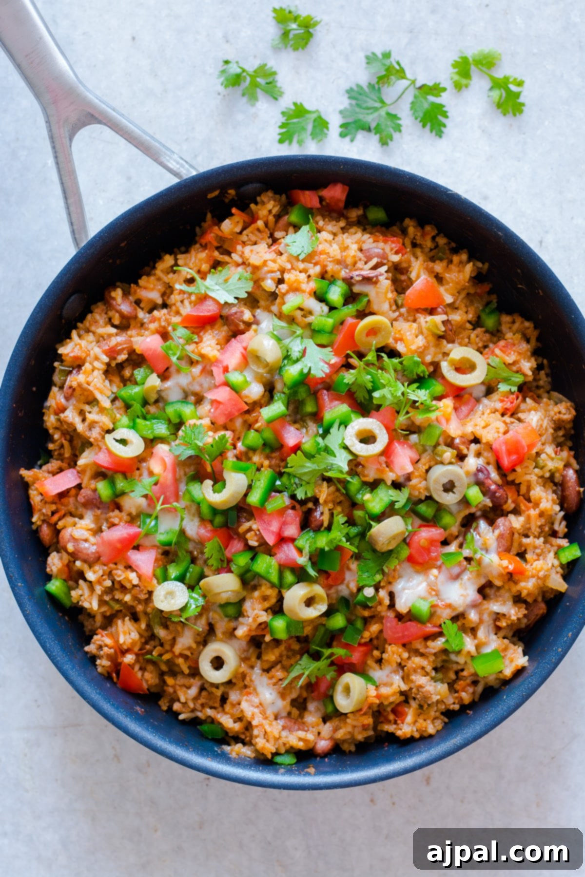 skillet with beef and rice, salsa, cilantro, jalapeno, and olives.