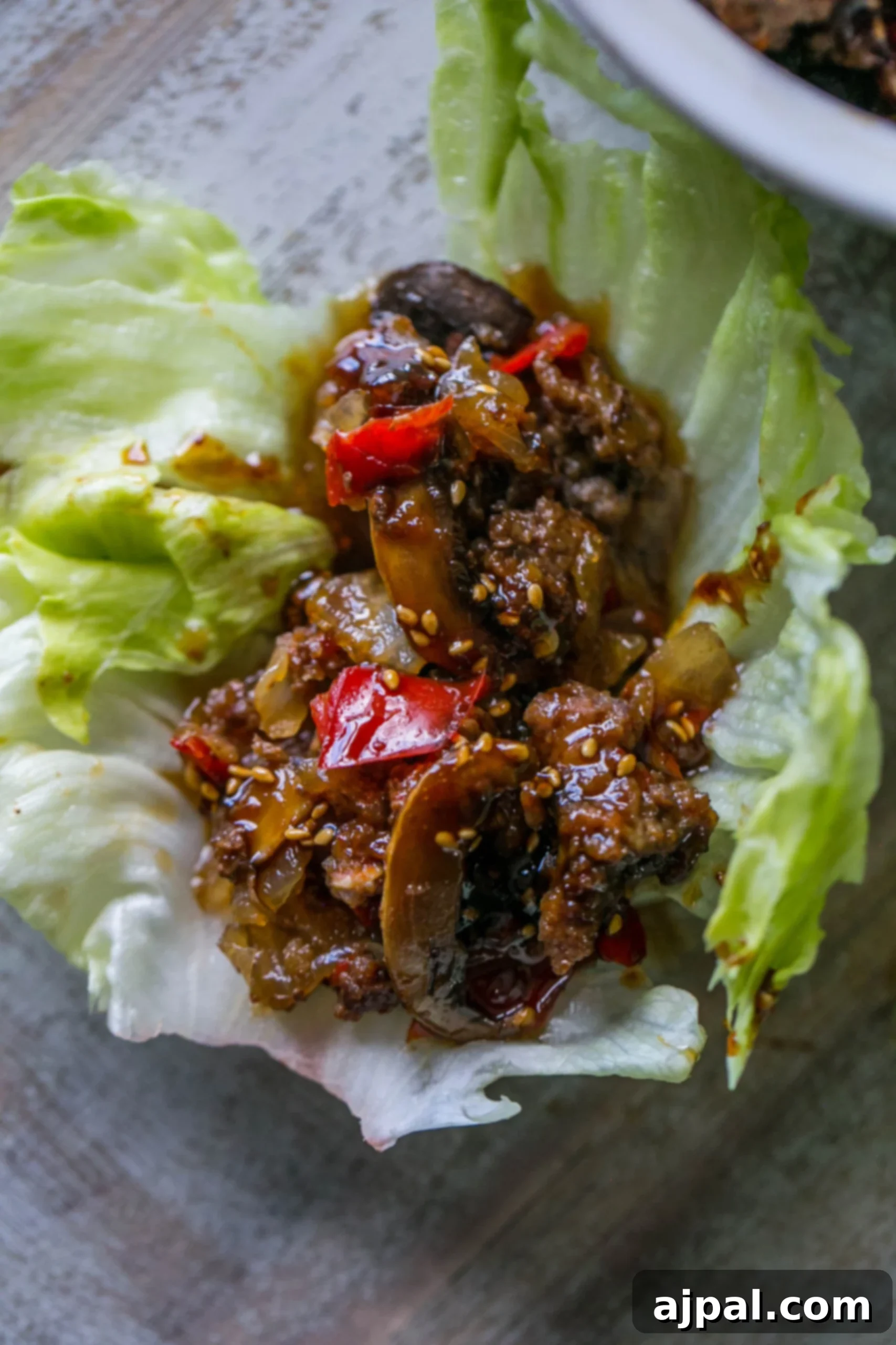 A close-up view of a sweet chili beef and mushroom lettuce wrap, sprinkled with white sesame seeds.