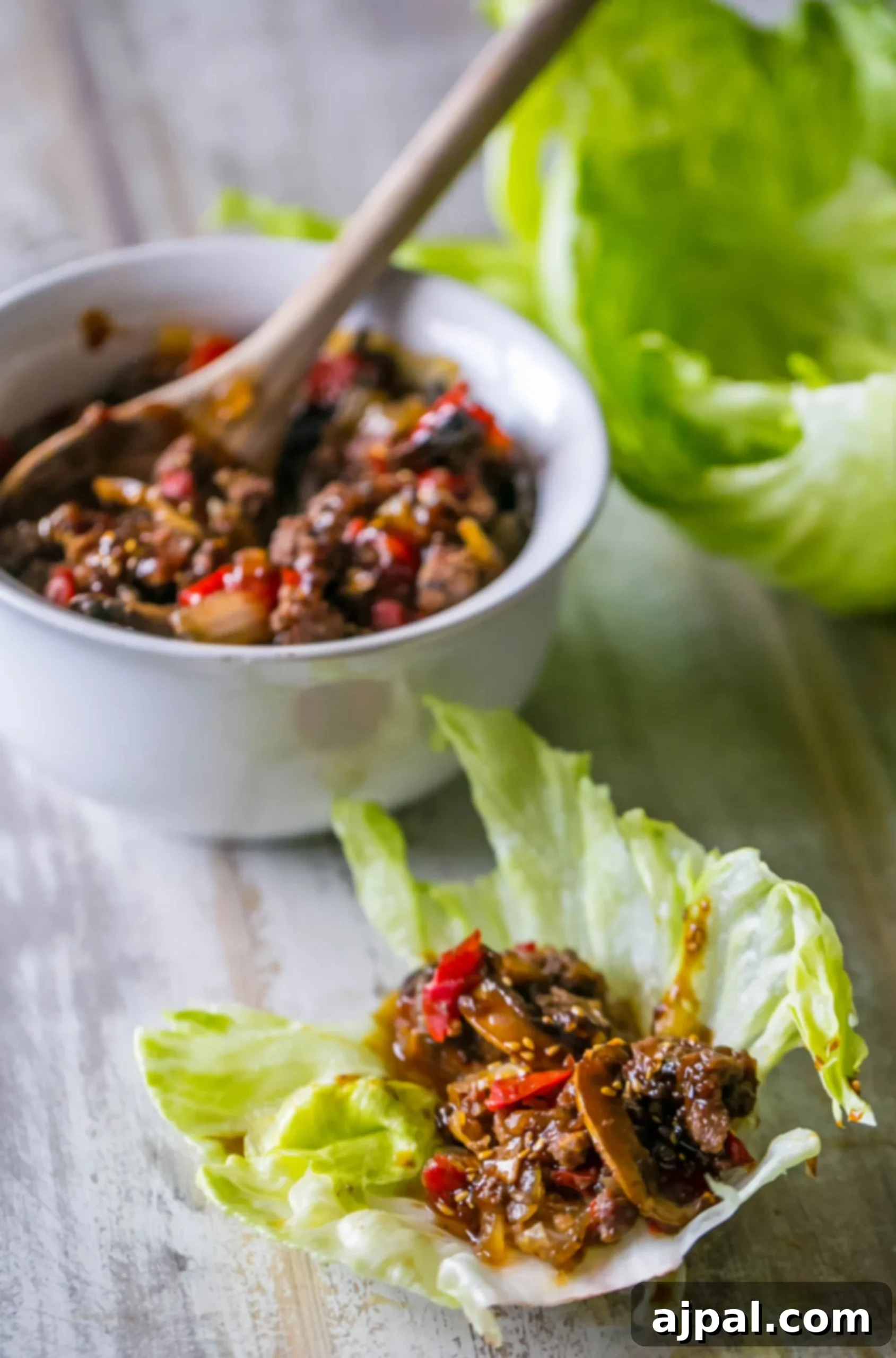 A delicious sweet chili beef and mushroom lettuce wrap, with a bowl of the filling in the background.
