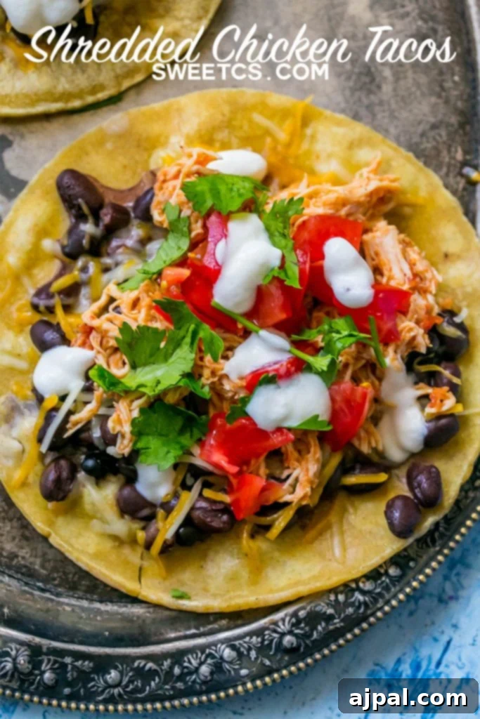 A vibrant platter of shredded chicken tacos, adorned with fresh toppings like sour cream, cilantro, black beans, and salsa, ready to be enjoyed.