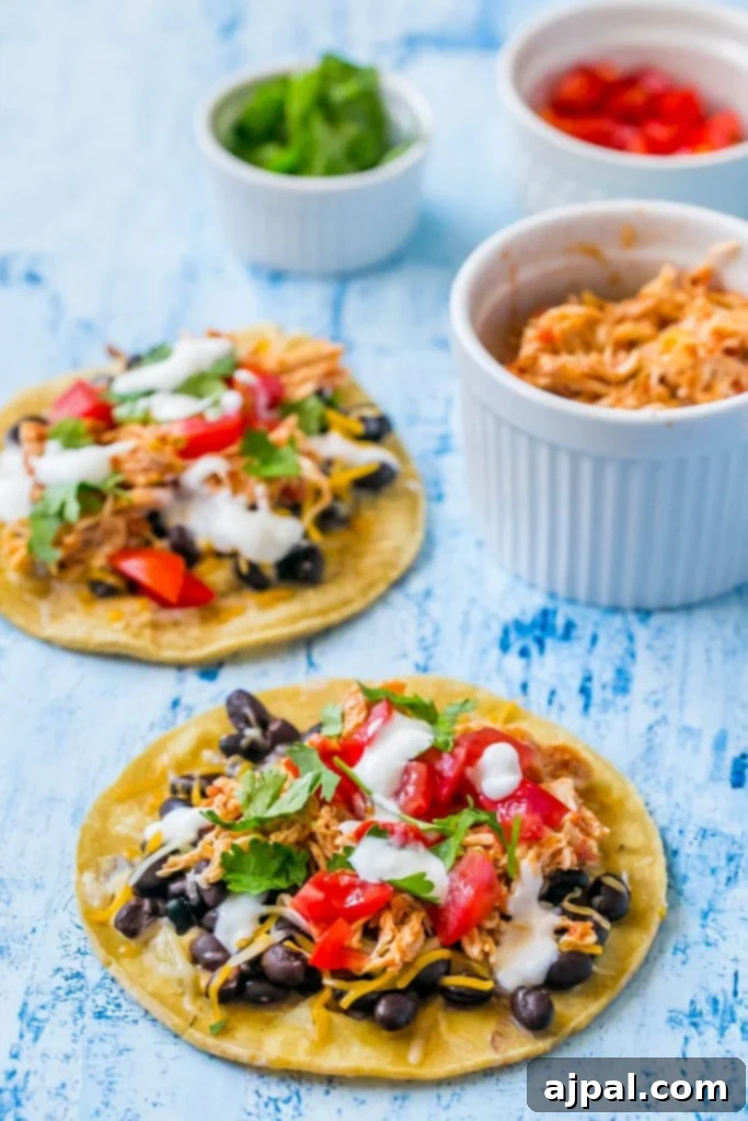 A close-up shot of a single shredded chicken taco, garnished with sour cream, cilantro, black beans, and salsa, on a textured blue surface.