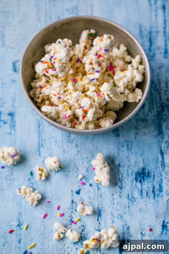 Birthday Cake Popcorn 3 Close-up of a bowl filled with vibrant white chocolate cake batter popcorn, generously adorned with sprinkles.