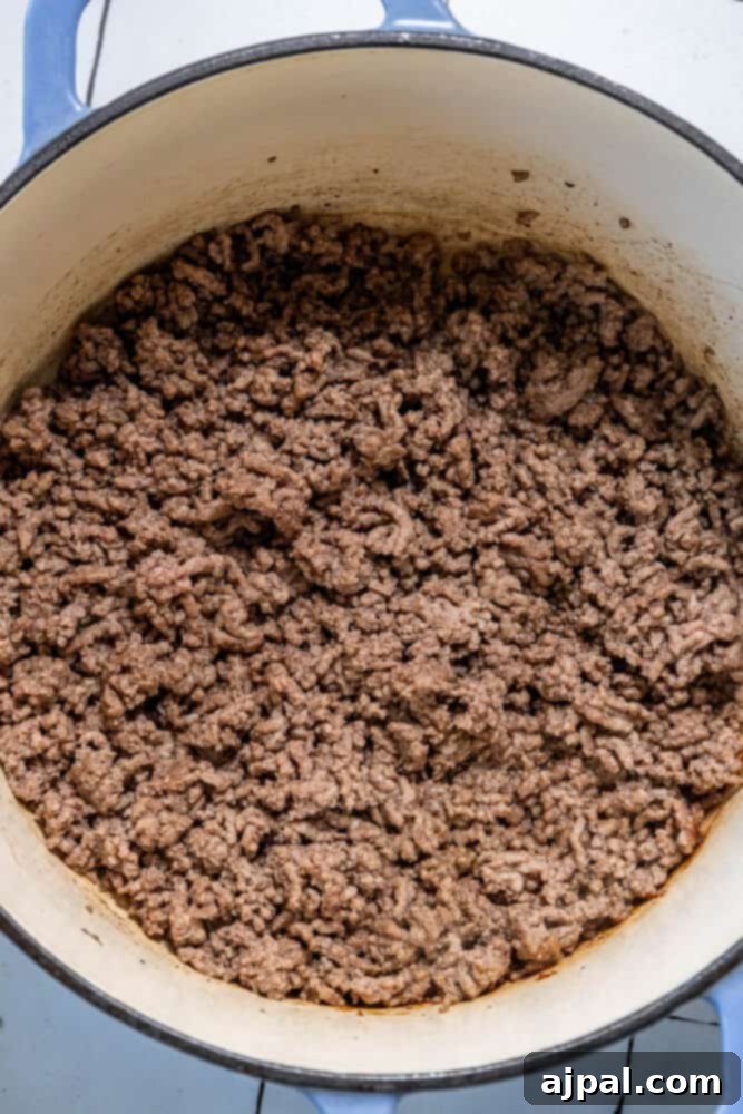 Ground beef browning in a large pan on a stovetop, ready for the next step in making a hearty cabbage soup.
