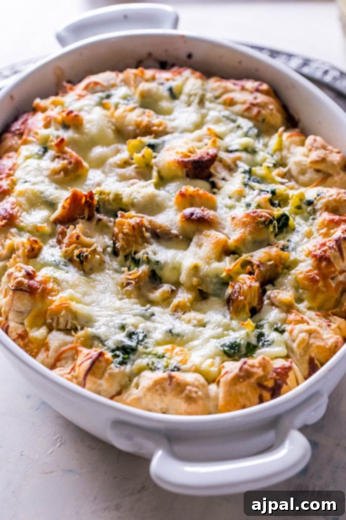 A picture of cheesy chicken, spinach, and artichoke bread dip in a white casserole dish, highlighting the texture and richness.