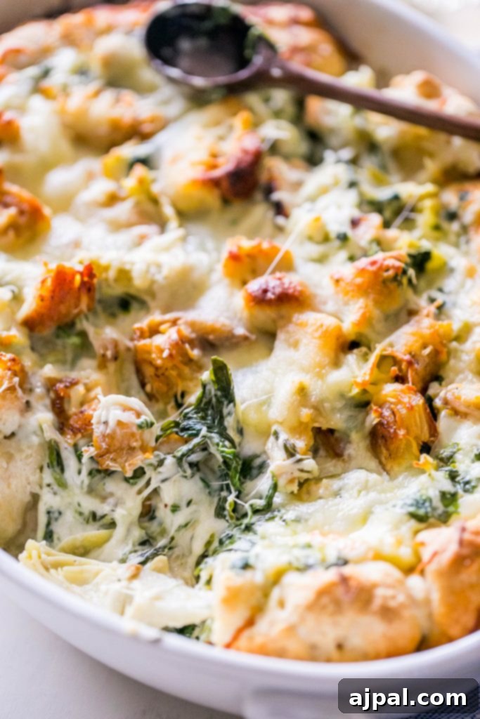 A close-up picture of the bubbling, golden-brown cheesy chicken, spinach, and artichoke bread dip in a white casserole dish.