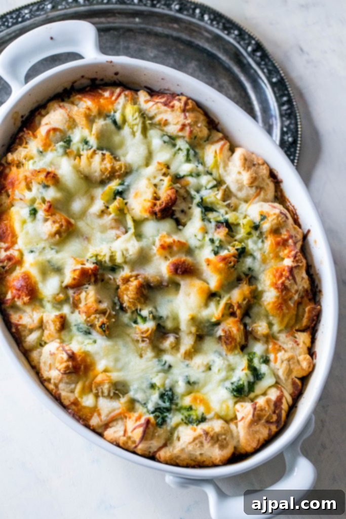 A picture of the cheesy chicken, spinach, and artichoke bread dip in a white casserole dish, showing the bread ring and the bubbling dip.